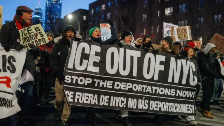 Gran grupo de manifestantes con pancartas en Minneapolis protestando contra políticas migratorias del gobierno de Trump, con ambiente urbano